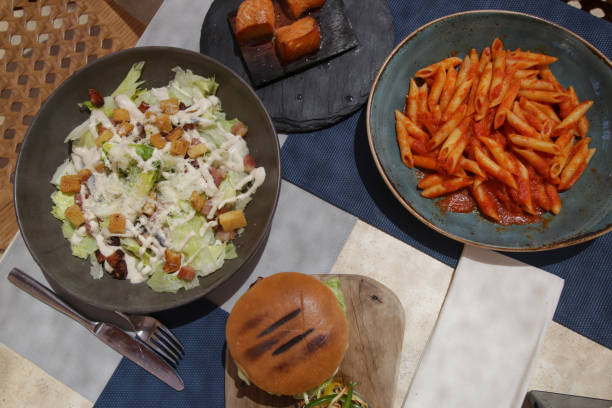 Different food served on the restaurant table, penne tomato pasta, hamburger and tuna salad Different food served on the restaurant table, penne tomato pasta, hamburger and tuna salad caesar salad food salad tuna stock pictures, royalty-free photos & images