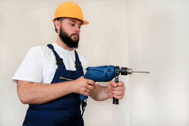 istock Construction worker and handyman works on renovation of apartment. Builder with blue electric drill drills a nail hole into wall of construction site. House renovation concept. Construction tools. 1170751011