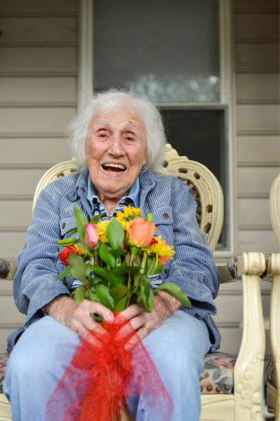 Happy Centenarian Woman A 103-year-old woman with Alzheimer's disease sits on porch chair, holds bouquet of flowers and smiles at camera. over 100 stock pictures, royalty-free photos & images
