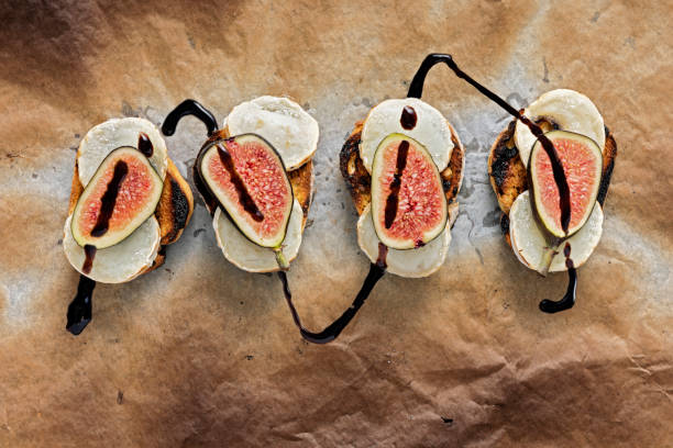 Fresh figs with melted goats cheese and balsamic vinegar on toasted bread. Overhead, close-up  view of fresh figs with melted goats cheese on top of toasted french bread with a delicate drizzle of balsamic vinegar. Colour, horizontal with some copy space. Photographed just as they come out of the grill with the cheese melting. vinegar stock pictures, royalty-free photos & images