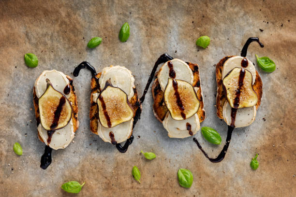 Fresh figs with melted goats cheese and balsamic vinegar on toasted bread. Overhead, close-up  view of fresh figs with melted goats cheese on top of toasted french bread with a delicate drizzle of balsamic vinegar, torn basil leaves and freshly ground pepper. Colour, horizontal with some copy space. Photographed just as they come out of the grill with the cheese melting. balsamic vinegar stock pictures, royalty-free photos & images