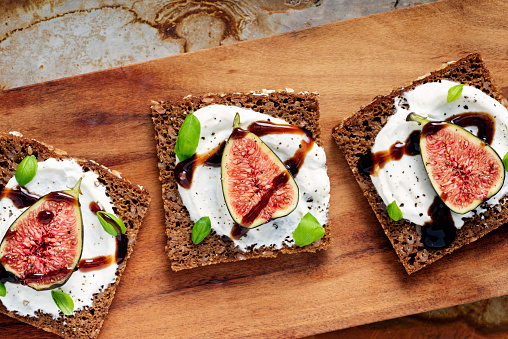 Overhead, close-up  view of fresh figs with ricotta cheese, fresh basil leaves on rye bread with a drizzle of balsamic vinegar. Colour, horizontal with some copy space.