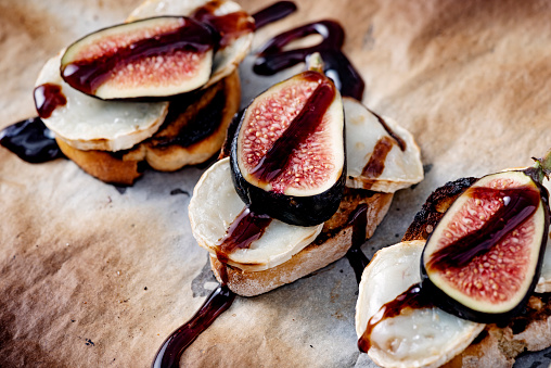 Close-up  view of fresh figs with melted goats cheese on top of a pice of toasted french bread with a delicate drizzle of balsamic vinegar. Colour, horizontal with some copy space. Photographed just as they come out of the grill with the cheese melting.