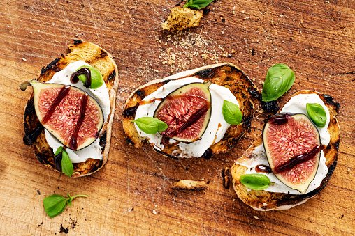 Overhead view of a selection of fresh figs with ricotta cheese, on toasted baguette with torn basil leaves and a delicate drizzle of balsamic vinegar. Colour, horizontal with some copy space.