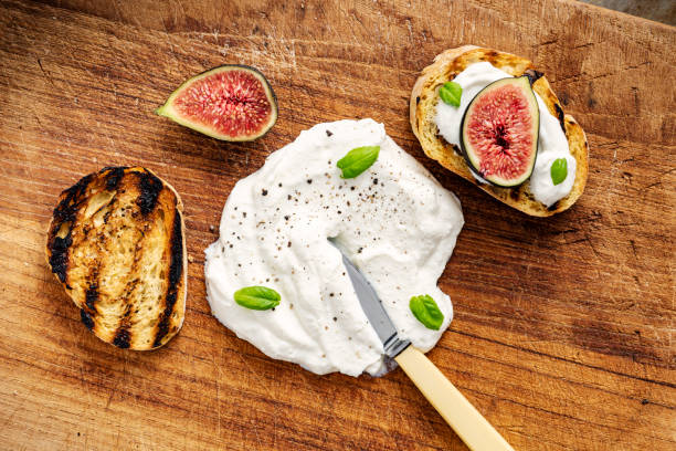 Fresh figs with ricotta cheese and fresh basil. Overhead view preparing a dish of fresh figs with ricotta cheese, on toasted baguette with torn basil leaves. Colour, horizontal with copy space. ricotta stock pictures, royalty-free photos & images