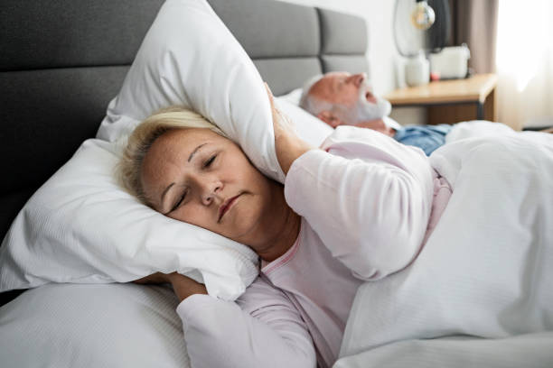 esposa bloqueando oídos con almohada mientras el marido roncan doña en el sueño - roncar fotografías e imágenes de stock