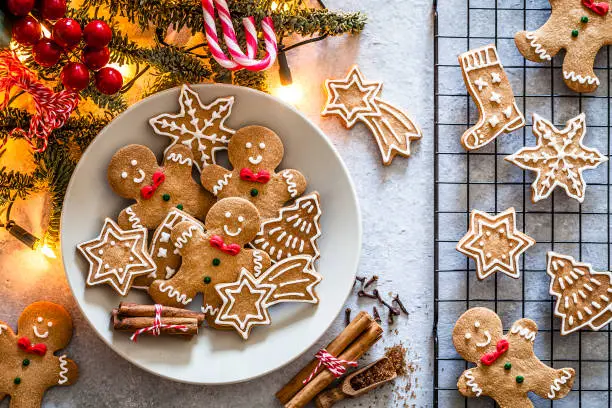 Top view of homemade Christmas cookies shot on gray Christmas table. Some cookies are on a gray plate and others on a cooling rack. Yellow Christmas lights and Christmas decoration complete the composition. Predominant colors are brown and gray. Low key DSRL studio photo taken with Canon EOS 5D Mk II and Canon EF 100mm f/2.8L Macro IS USM