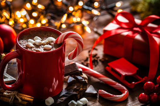 Homemade hot chocolate mug with red and white candy cane on rustic wooden Christmas table
