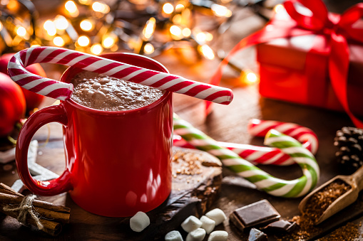 Homemade hot chocolate mug with red and white candy cane on rustic wooden Christmas table