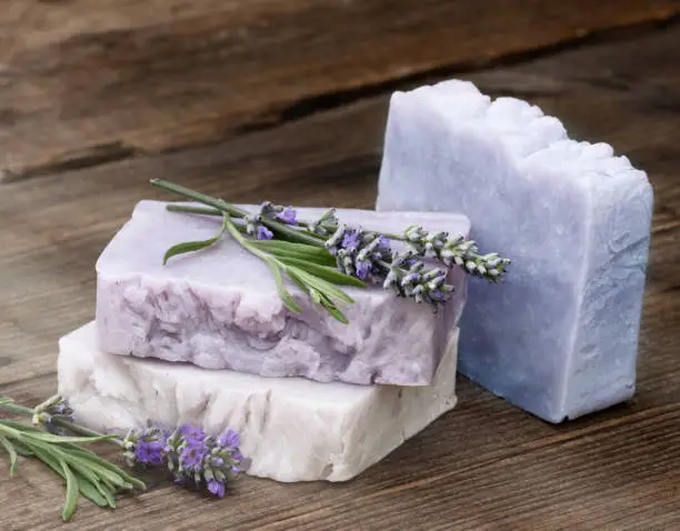 Handmade bars of Soap with lavender flowers on rustic wooden table.