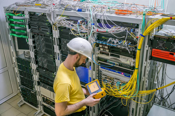 The engineer in a white helmet measures the level of the optical signal in the server room of the data center. A technician diagnoses a problem area in a telecommunication network. The engineer in a white helmet measures the level of the optical signal in the server room of the data center. A technician diagnoses a problem area in a telecommunication network. computer network router communication internet stock pictures, royalty-free photos & images