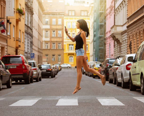 Woman crossing street, jumping, checking phone Woman crossing street, jumping, checking phone hopper car stock pictures, royalty-free photos & images