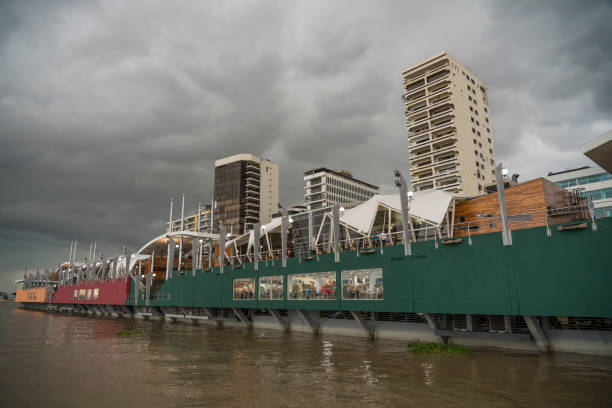 Unrecognizable people in restaurant at waterfront at the river, skyscrapers in background against overcast sky.