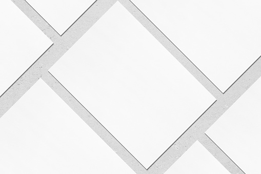 Closeup of empty white rectangle poster mockups lying diagonally with soft shadow on neutral light grey concrete background. Flat lay, top view. Open composition.