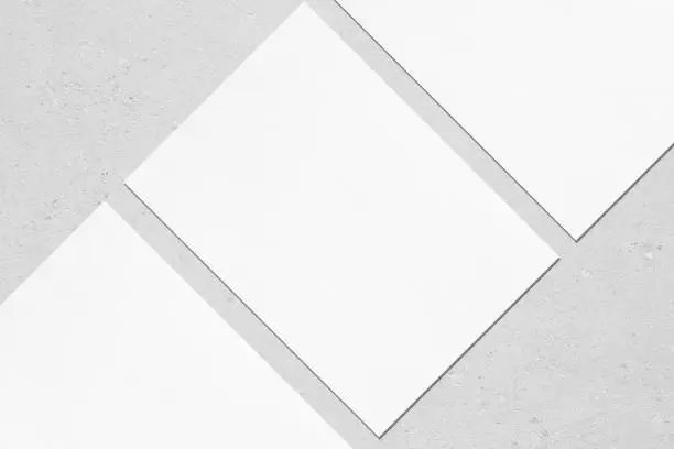 Photo of Close up of three empty white rectangle poster mockups lying diagonally on grey concrete background