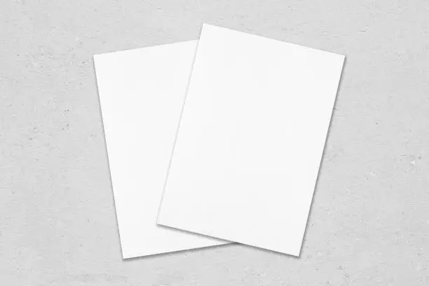 Photo of Two empty white poster mockups lying diagonally on top of each other on grey concrete background