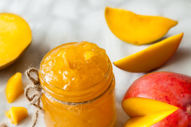 Mango homemade jam with raw slice fresh ripe tropical fruit on marble table, selective focus top view stock photo