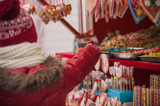 A child in red jacket and cap is pointing at multi-colored candies on a Christmas market.