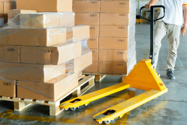istock warehouse worker working with hand pallet truck or hand lift pallet jack, stack cardboard boxes on wooden pallet at distribution warehouse. 1170813134