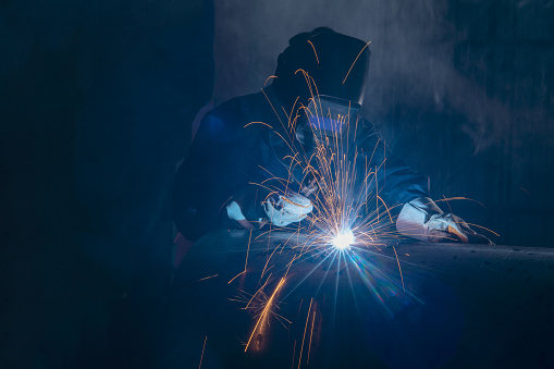 Professional welder and mask welding metal pipe on the industrial table.