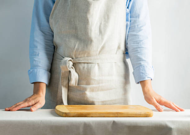Female cook in cotton apron at the kitchen table with cutting board. Rustic natural style. Kinfolk concept. Copy space.