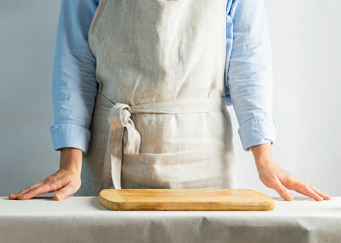 Female cook in a cotton apron at the kitchen table with cutting board. Rustic natural style. Kinfolk concept. Copy space. Horizontal frame