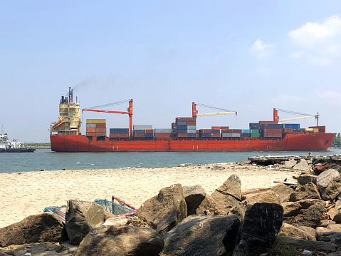 Stock photo of huge cargo ship entering the Kochin port for cargo loading / unloading down the sea channel, ship is being moored by a tug boat to get into port side Kochi port, Kerala, India