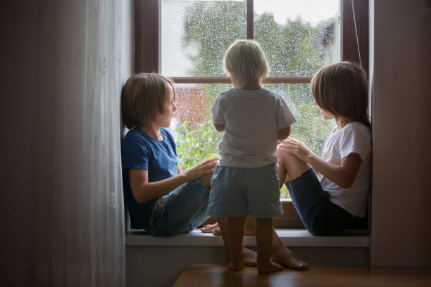 istock Happy siblings, boy brothers, sitting on a window shield on a rainy day, playing together 1170826743