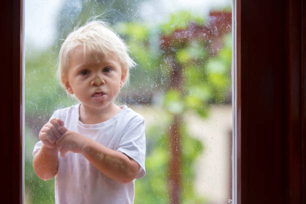 istock Cute little boy, looking at camera through glass door with rain drops, making faces 1170827021