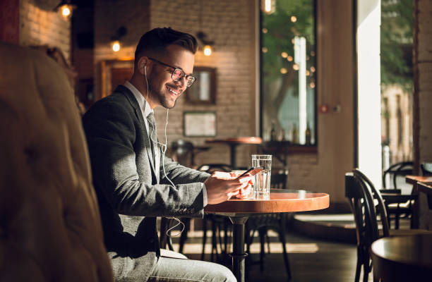 istock Businessman on a coffee break in cafe using phone with headphones smiling 1170834748