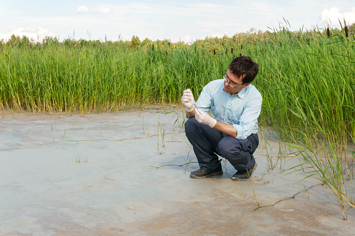 field researcher biologist examines a sample of soil in a test tube against a dry marsh