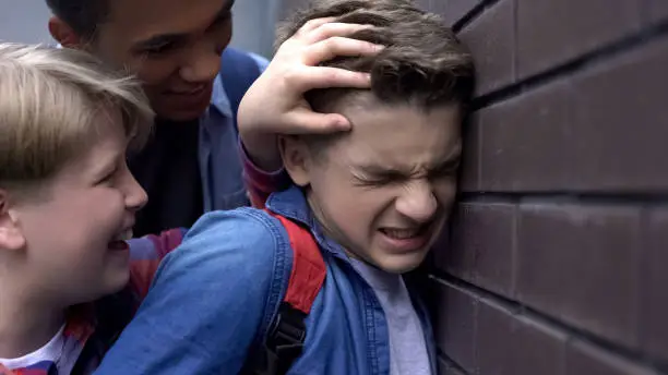 Cruel teenagers bullying, pushing classmate to wall, threatening physical harm