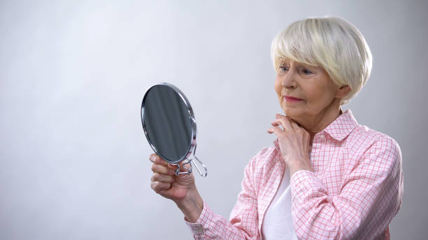 istock Elderly woman looking at wrinkled face in mirror, thinking about plastic surgery 1170853614