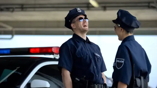 Photo of Young police officers laughing standing near car, successful patrol shift