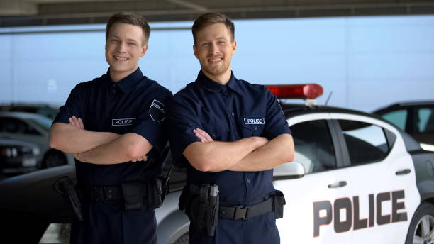 istock Smiling policemen with hands crossed standing against squad car on background 1170854297