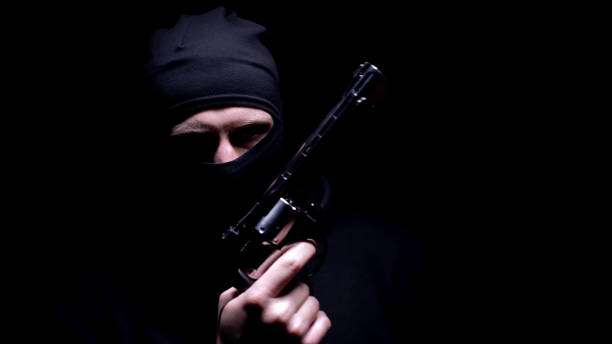 istock Dangerous man in balaclava mask holding gun, black background, serial killer 1170854868