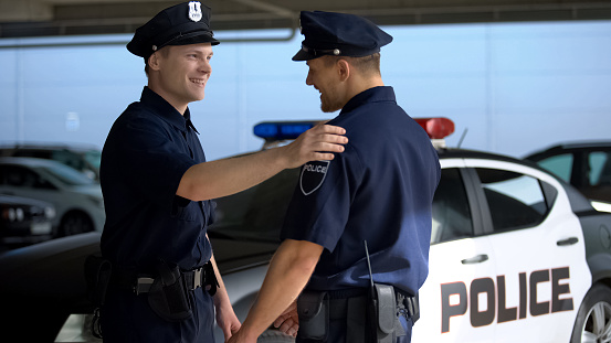 Cheerful policeman greeting mate against squad car, ready for patrolling, work