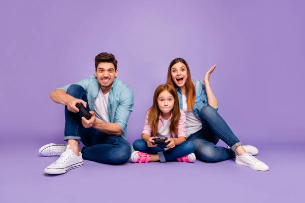 Photo of three family members sitting floor trying hard to win team game wear casual clothes isolated purple background Photo of three family members, sitting floor trying hard to win team game wear casual clothes isolated purple background gamepad photos stock pictures, royalty-free photos & images
