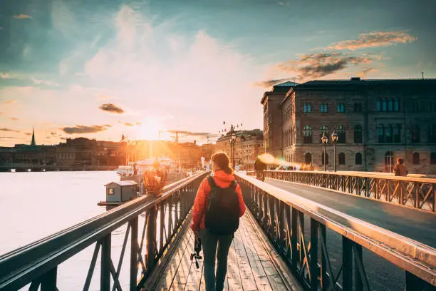 Photo of Stockholm, Sweden. Young Caucasian Woman Lady Tourist Traveler Walking On Famous Skeppsholmsbron - Skeppsholm Bridge. Popular Place, Landmark  And Destination In Stockholm, Sweden