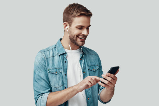 istock Handsome young man smiling and listening music while standing against grey background 1170873778