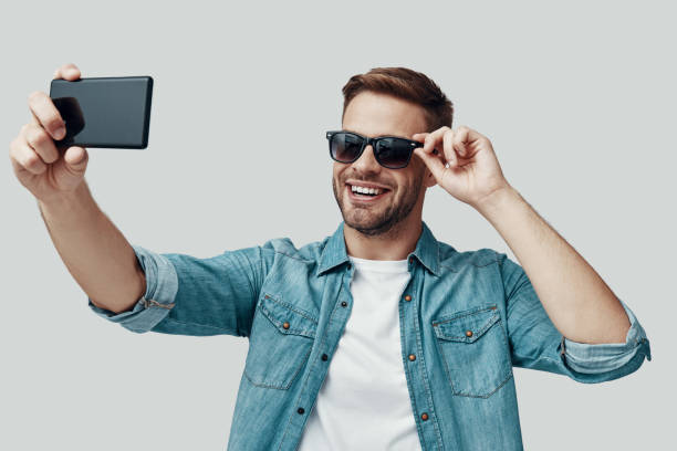 istock Handsome young man taking selfie using smart phone and smiling while standing against grey background 1170874396
