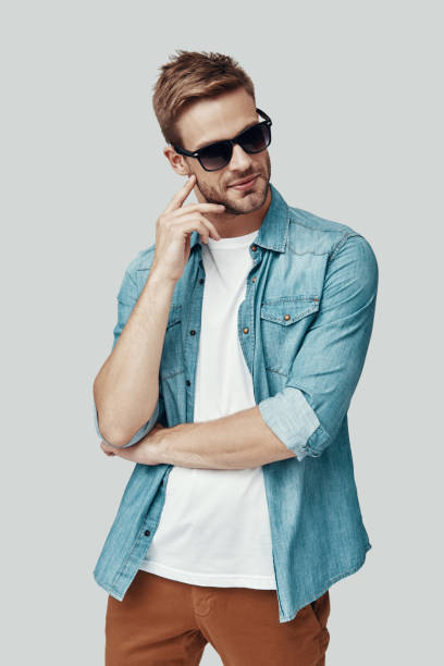 Handsome young man looking away and smiling while standing against grey background