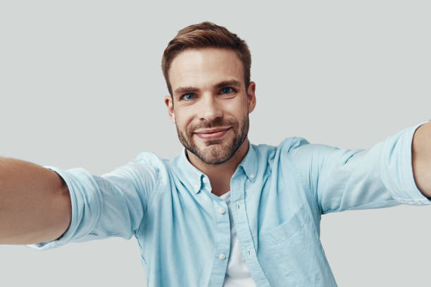 istock Self portrait of handsome young man looking at camera and smiling while standing against grey background 1170874943