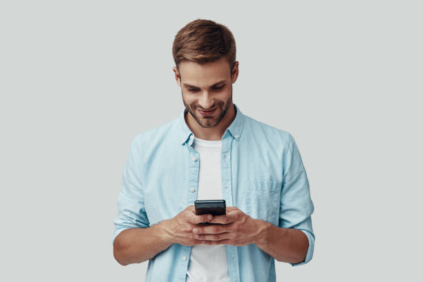 istock Handsome young man using smart phone and smiling while standing against grey background 1170875020