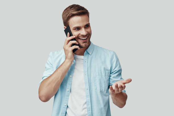 istock Handsome young man talking on the phone and smiling while standing against grey background 1170875608