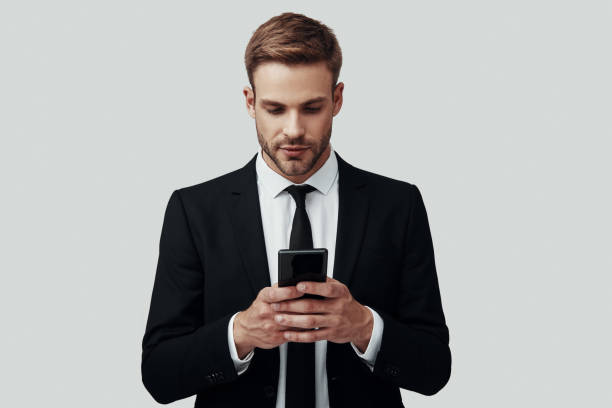 istock Handsome young man in formalwear using smart phone while standing against grey background 1170876173