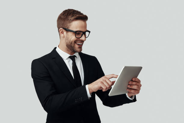 istock Handsome young man in formalwear working using digital tablet and smiling while standing against grey background 1170877629