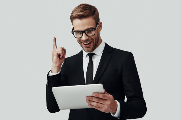 istock Handsome young man in formalwear working using digital tablet and smiling while standing against grey background 1170878704