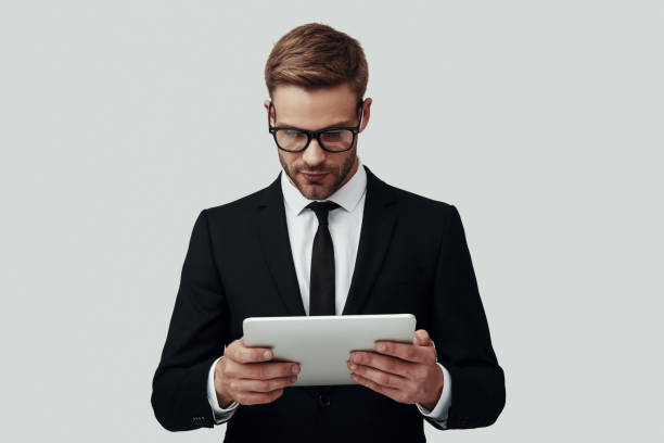 istock Handsome young man in formalwear working using digital tablet while standing against grey background 1170878841