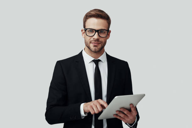 istock Handsome young man in formalwear working using digital tablet while standing against grey background 1170879024